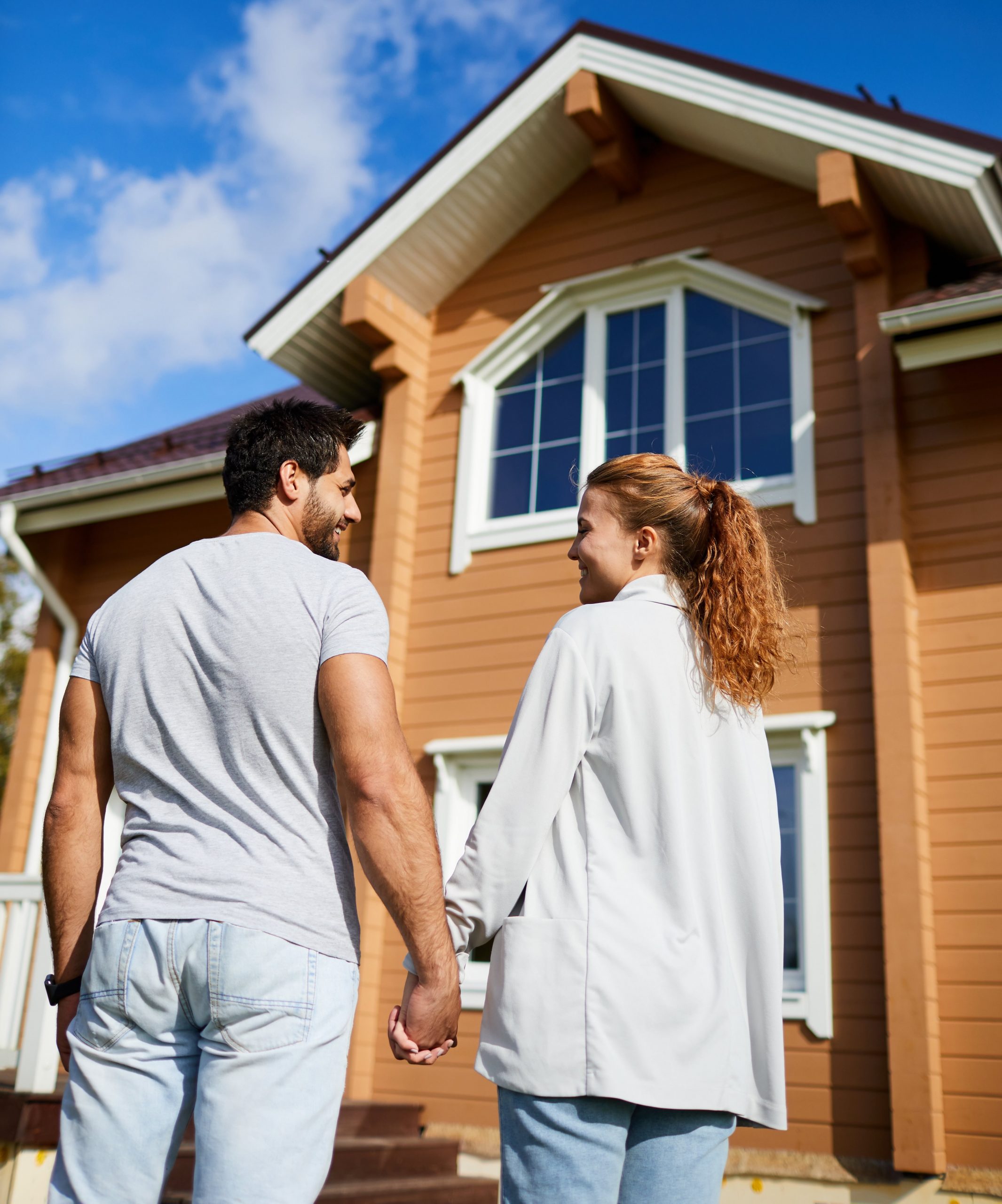 Back view of new owners of house standing in front of it anad looking at one another